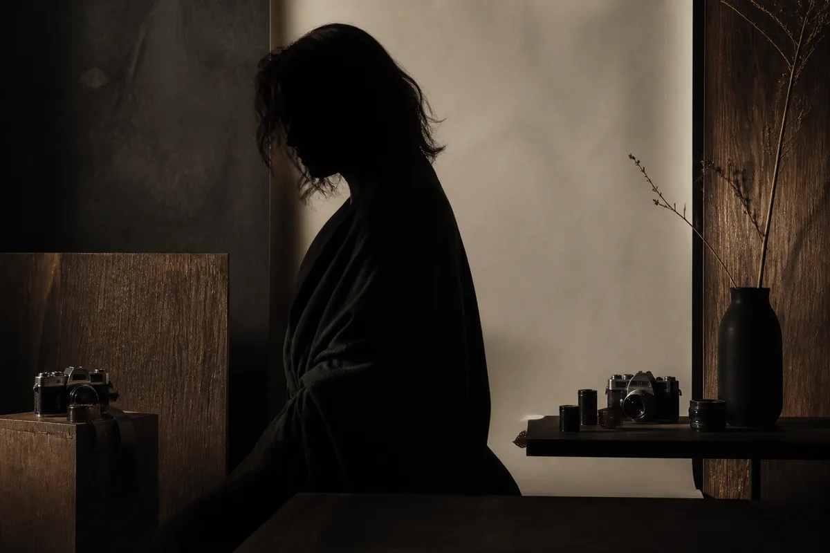 Portrait en clair-obscur, silhouette drapée devant un fond sombre texturé