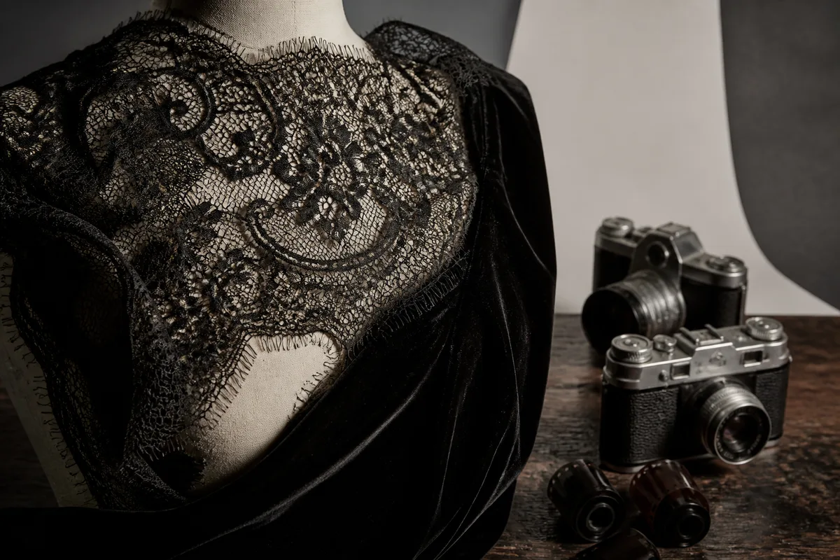 Détail de dentelle noire et de velours sur un buste, lumière rasante