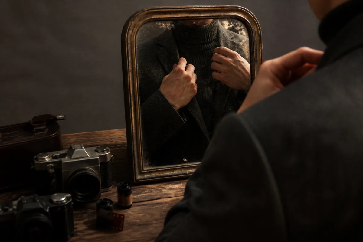 Mains d&rsquo;une personne ajustant le col d&rsquo;une veste devant un miroir ancien