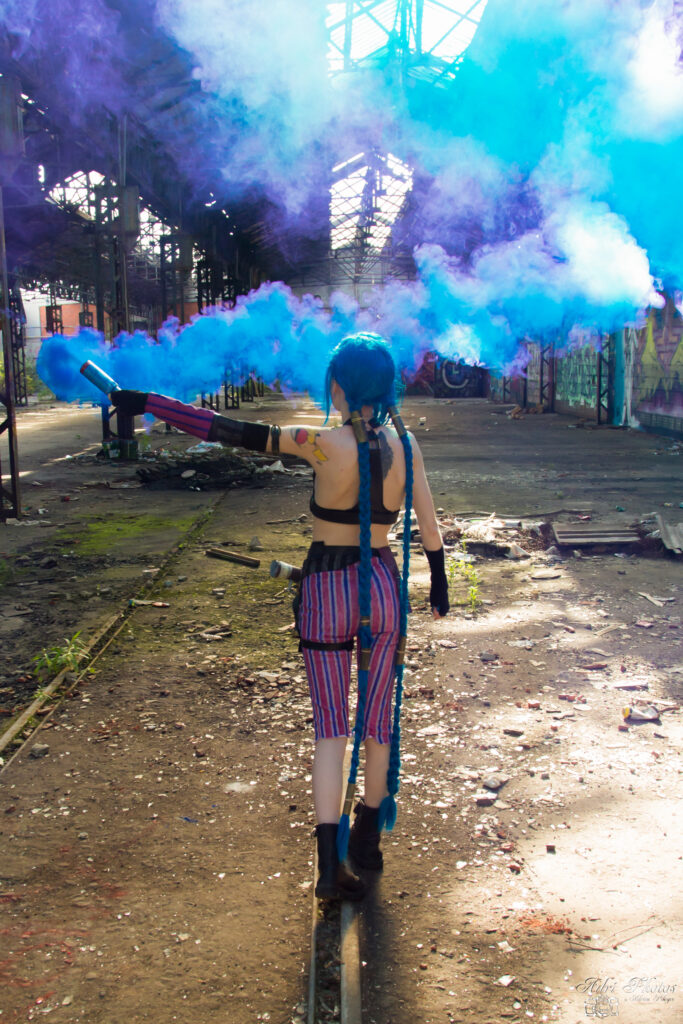 Cosplayeuse de Jinx marchant sur rail dans hanger avec fumigène bleu