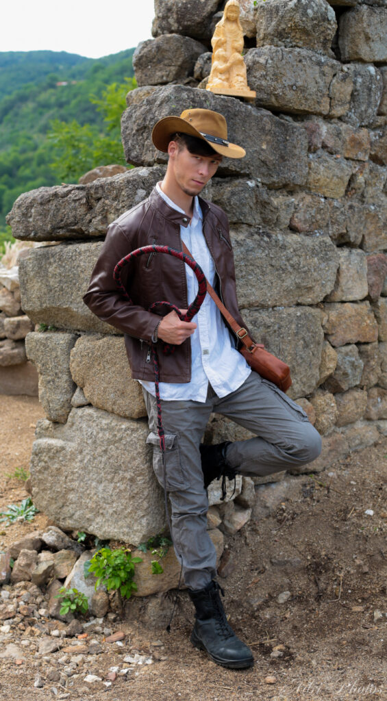 Indy pose contre un mur de pierre en ruine avec son fouet à la main